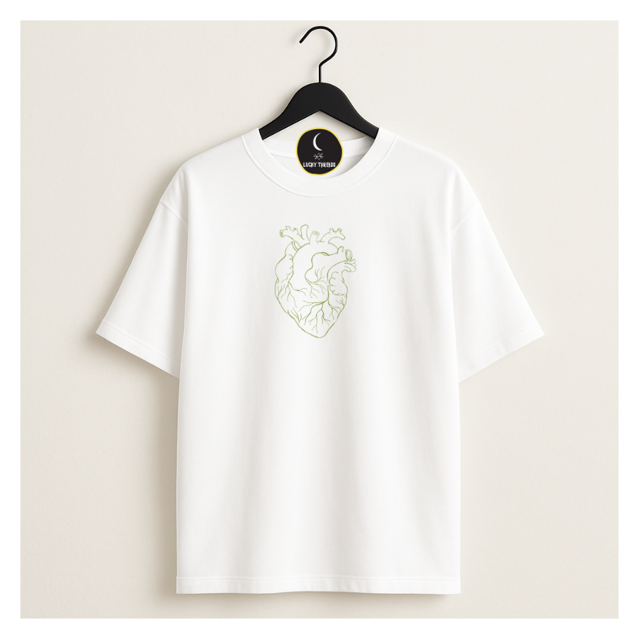 White short‑sleeved T‑shirt hanging on a black hanger against a beige background, featuring a minimalist light‑green line‑art anatomical heart printed on the chest. A circular Lucky Threads tag with a crescent moon logo hangs from the hanger.