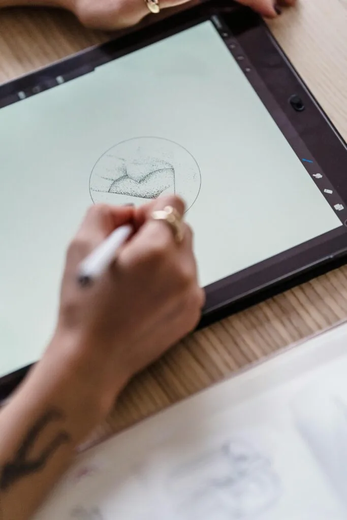 A close-up of an artist's hand sketching on a digital tablet in a creative workspace.